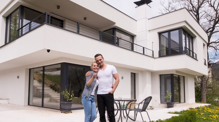 Couple de propriétaires souriants devant leur maison contemporaine